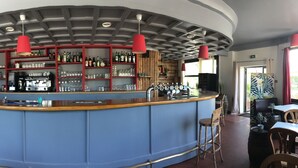A bar area with a wooden wall, a blue counter, and red pendant lights.