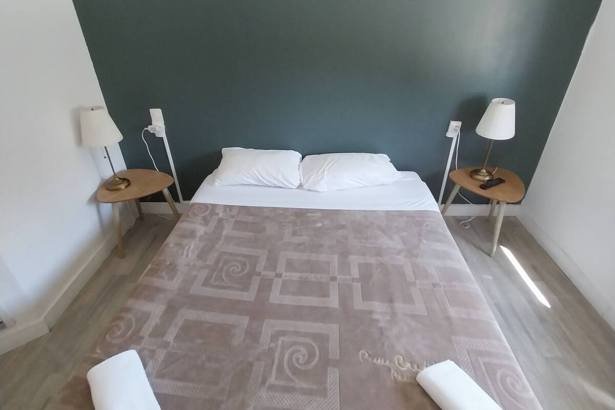 A bedroom with a bed, two bedside tables, a wall-mounted picture, and a patterned bedspread.