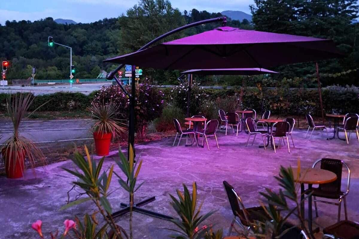 An outdoor patio with tables and chairs, surrounded by potted plants and a purple canopy.