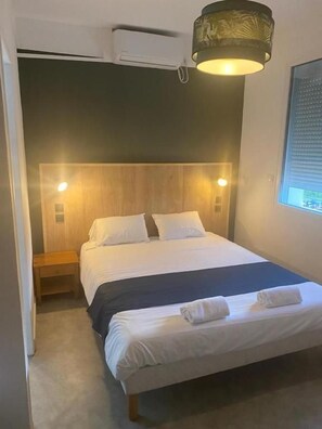 Una habitación de hotel con cama, mesitas de noche, una ventana y un aire acondicionado de pared.