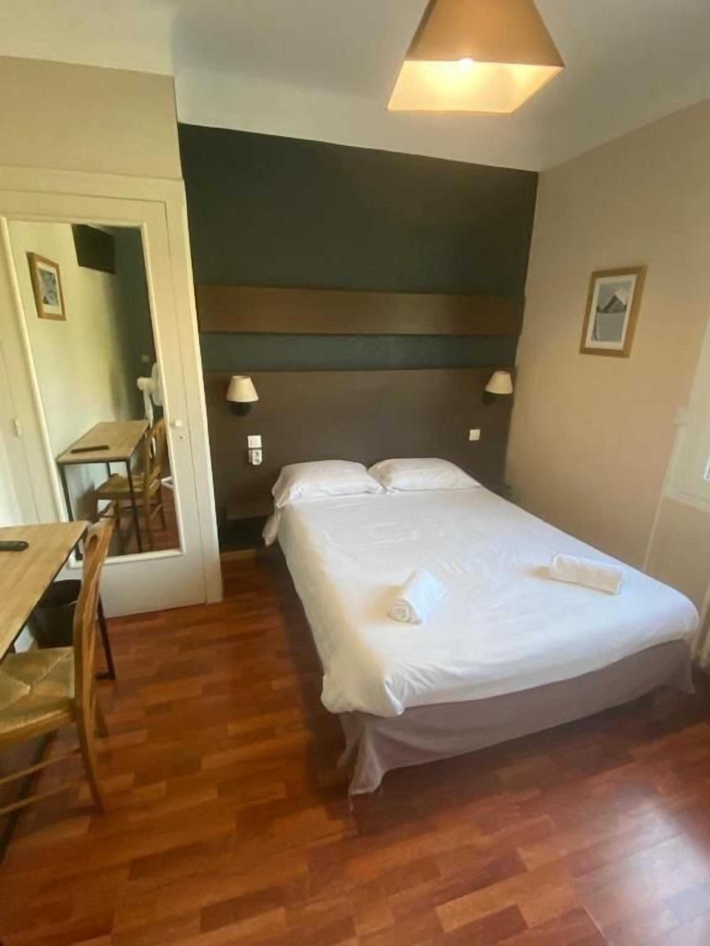 Una habitación de hotel con cama, lámparas de noche, piso de madera, escritorio y una silla.