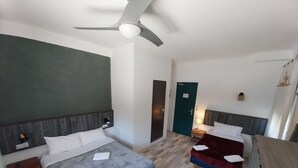 A hotel room with two beds, a ceiling fan, a wooden floor, and a green door.