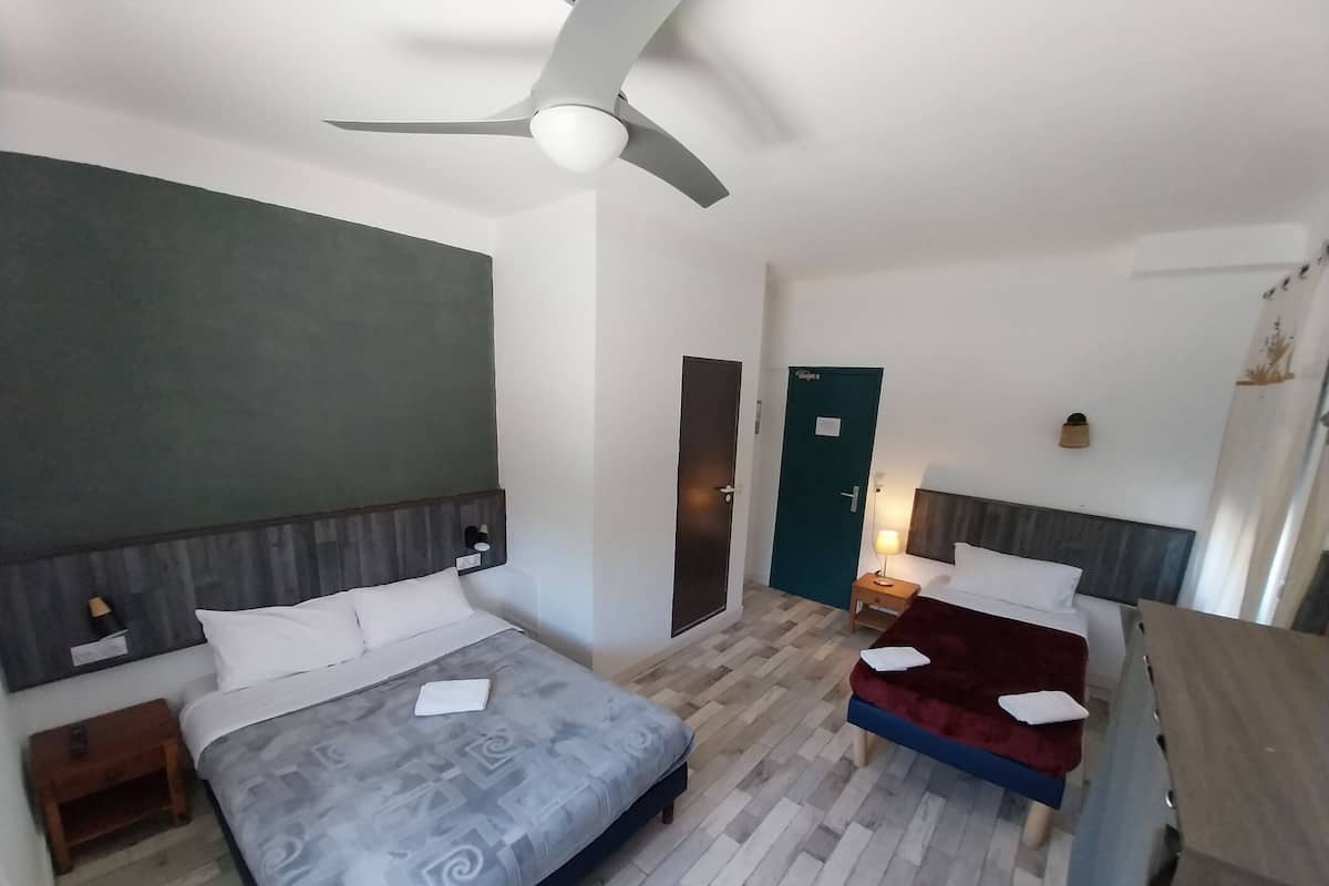 A hotel room with two beds, a ceiling fan, a wooden floor, and a green door.
