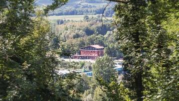 A red building with a flat roof, surrounded by dense trees and a hilly landscape.