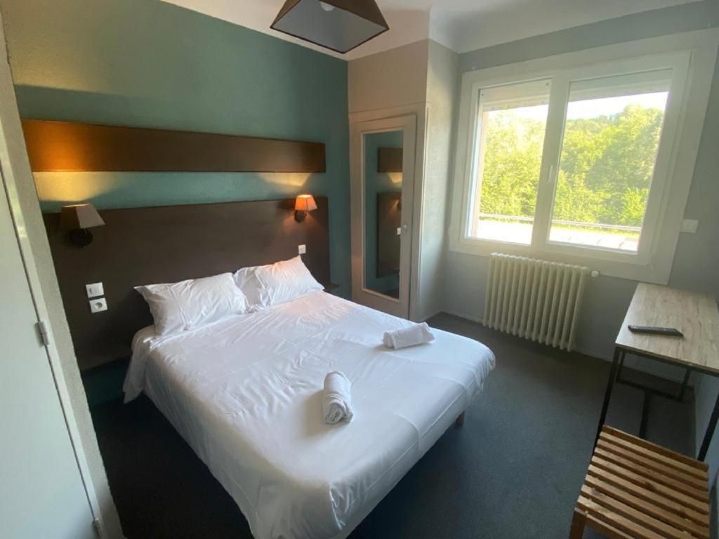 Quarto de hotel com cama, luminárias de cabeceira, janela, radiador e uma pequena mesa.