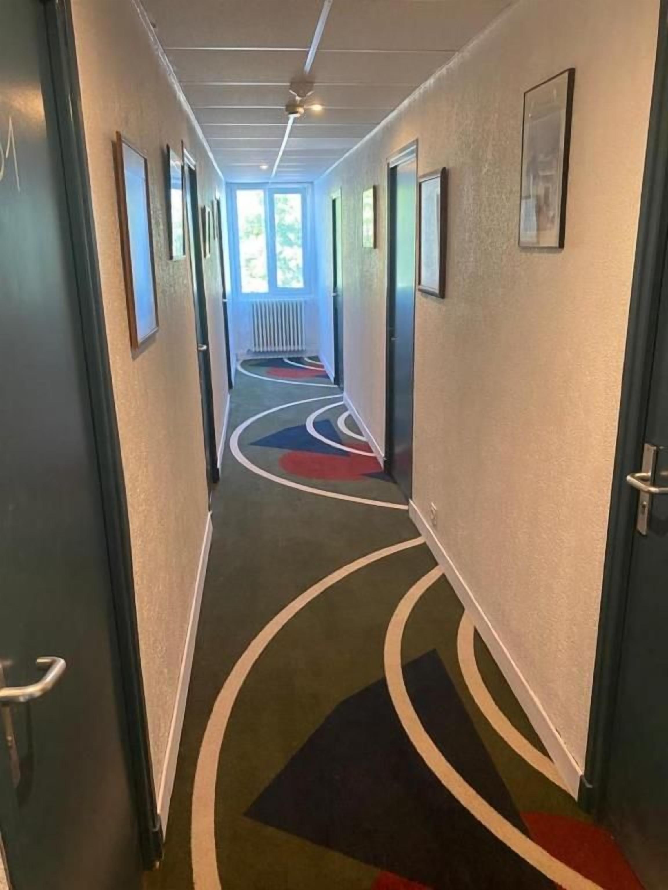 Un pasillo de hotel con piso alfombrado, puertas e imágenes enmarcadas en las paredes.