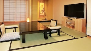 A traditional Japanese tatami room with a low table, two tatami mats, a television, and a sliding door.