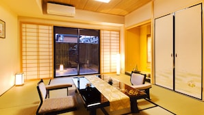 A traditional Japanese room with tatami flooring, a low table with cushions, a sliding door, and a view of the outside.