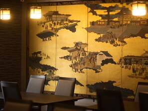 A traditional Japanese interior with tatami flooring, low tables, and a decorative wall with a historical scene. - Ryokan KANADE (Kyoto)
