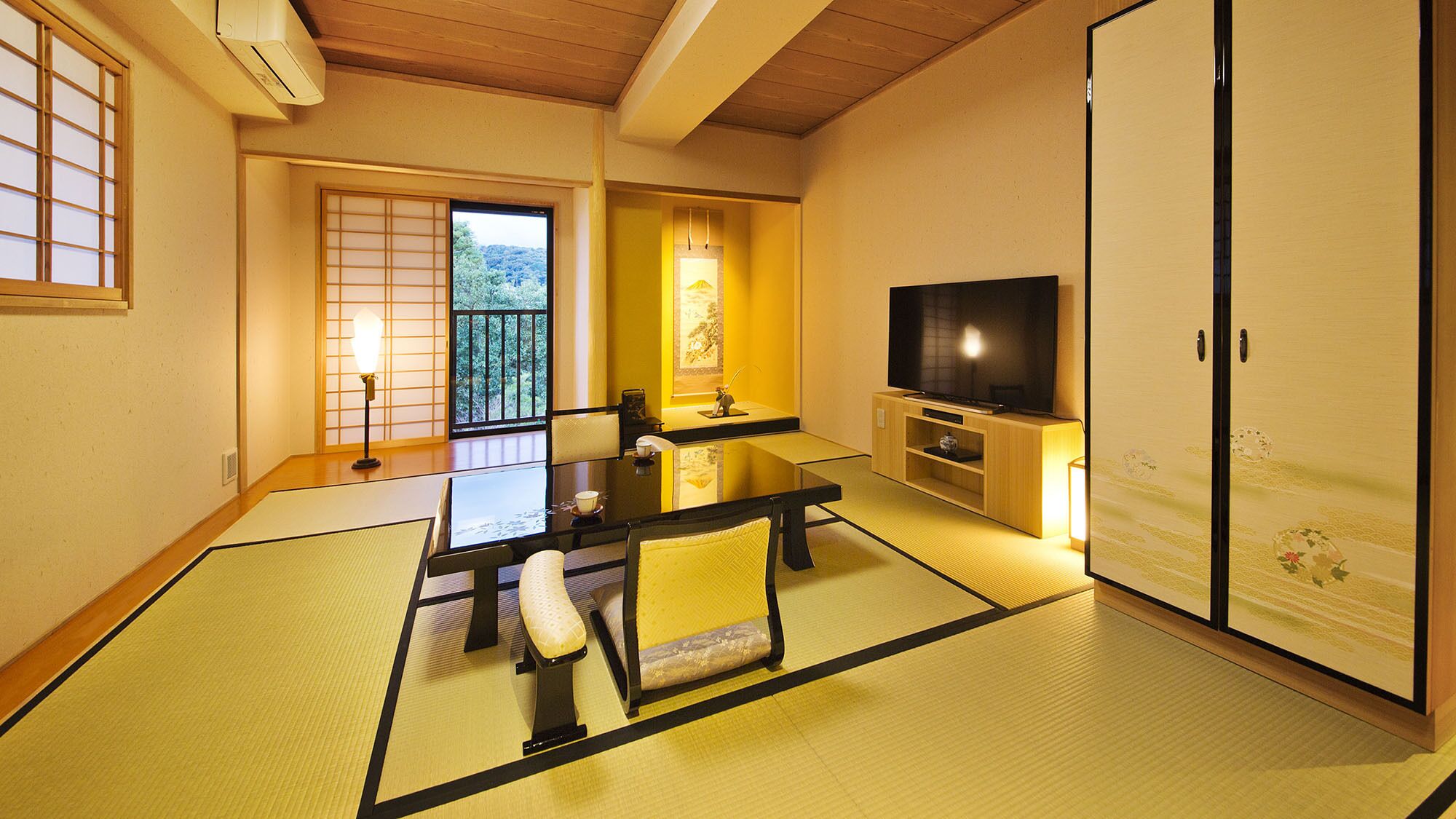 A traditional Japanese-style room with tatami flooring, a low table, a television, and sliding doors.