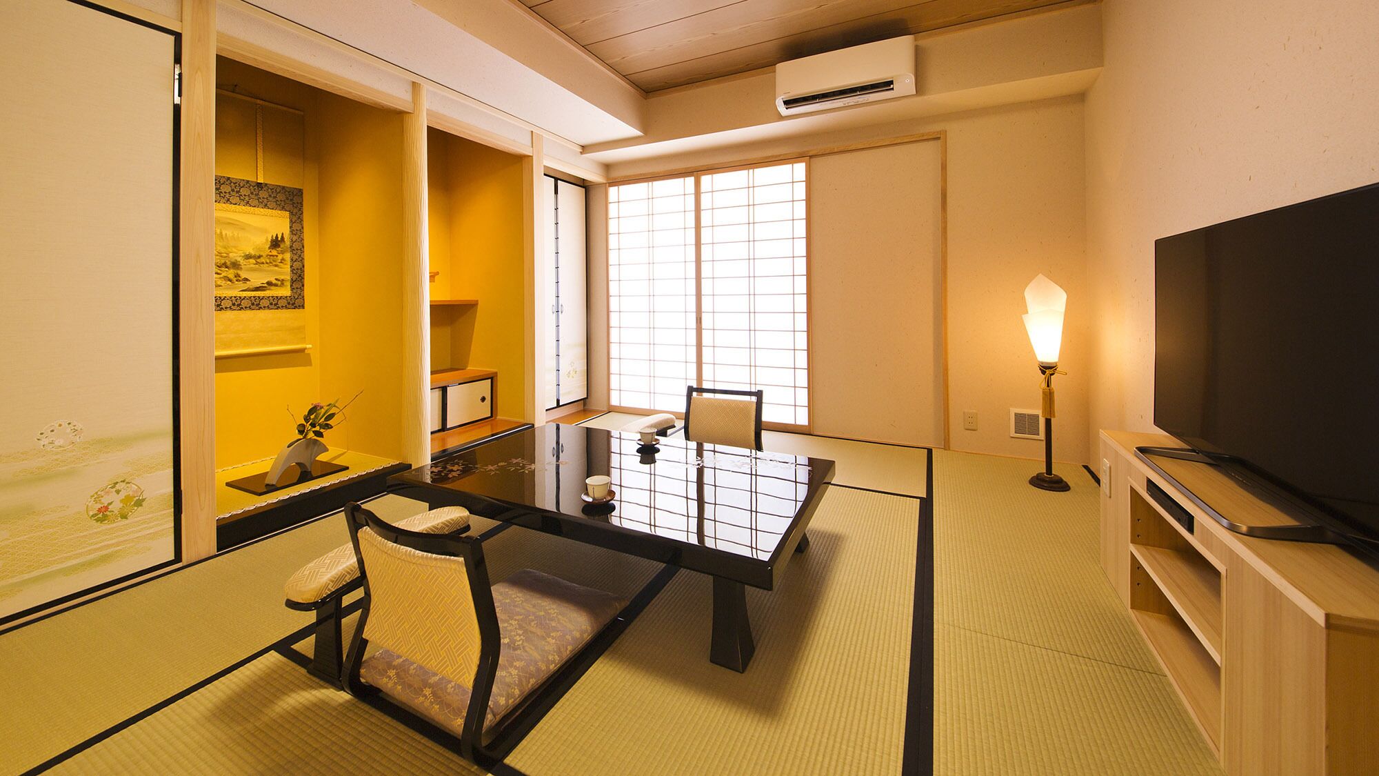 A traditional Japanese-style room with tatami flooring, a low table with a cushion, a television, and a lamp.