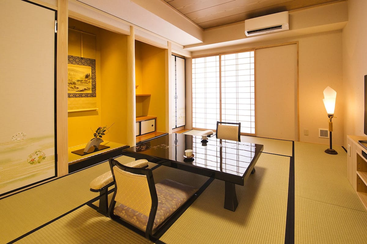 Une pièce de style japonais traditionnel, avec un sol recouvert de tatamis, une petite table basse avec un coussin, une télévision et une lampe.