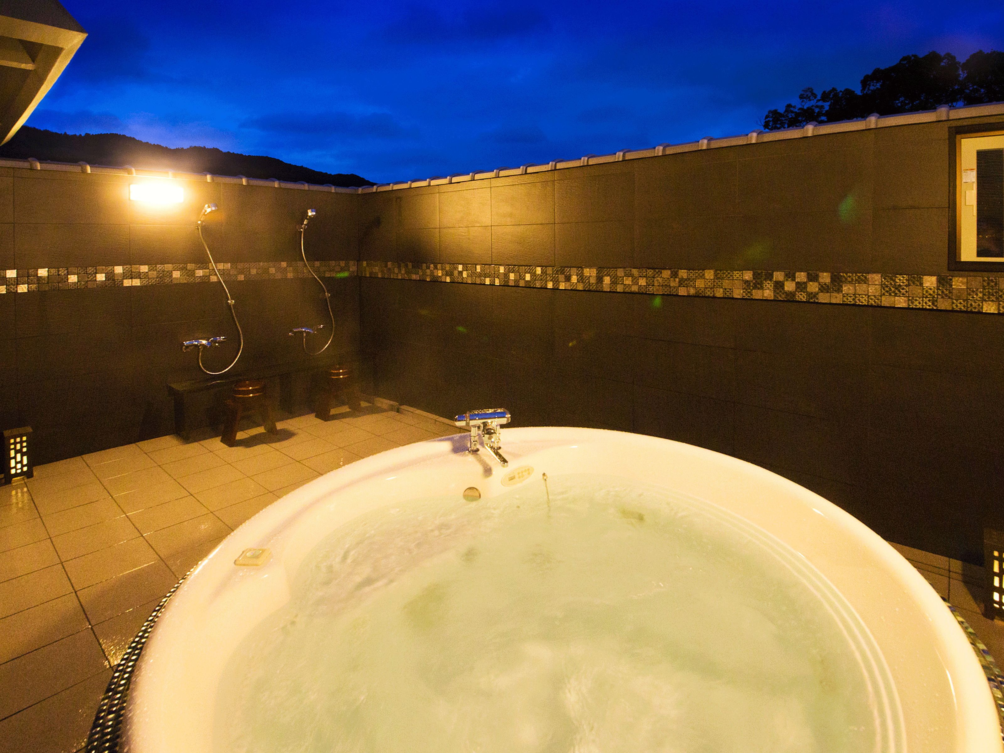 Un área de spa con un jacuzzi grande, ducha y pared de azulejos con un borde de mosaico.