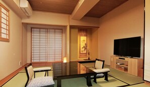 A traditional Japanese-style room with tatami flooring, a low table, two tatami mats, a television, and a sliding door with a view of a mountain.