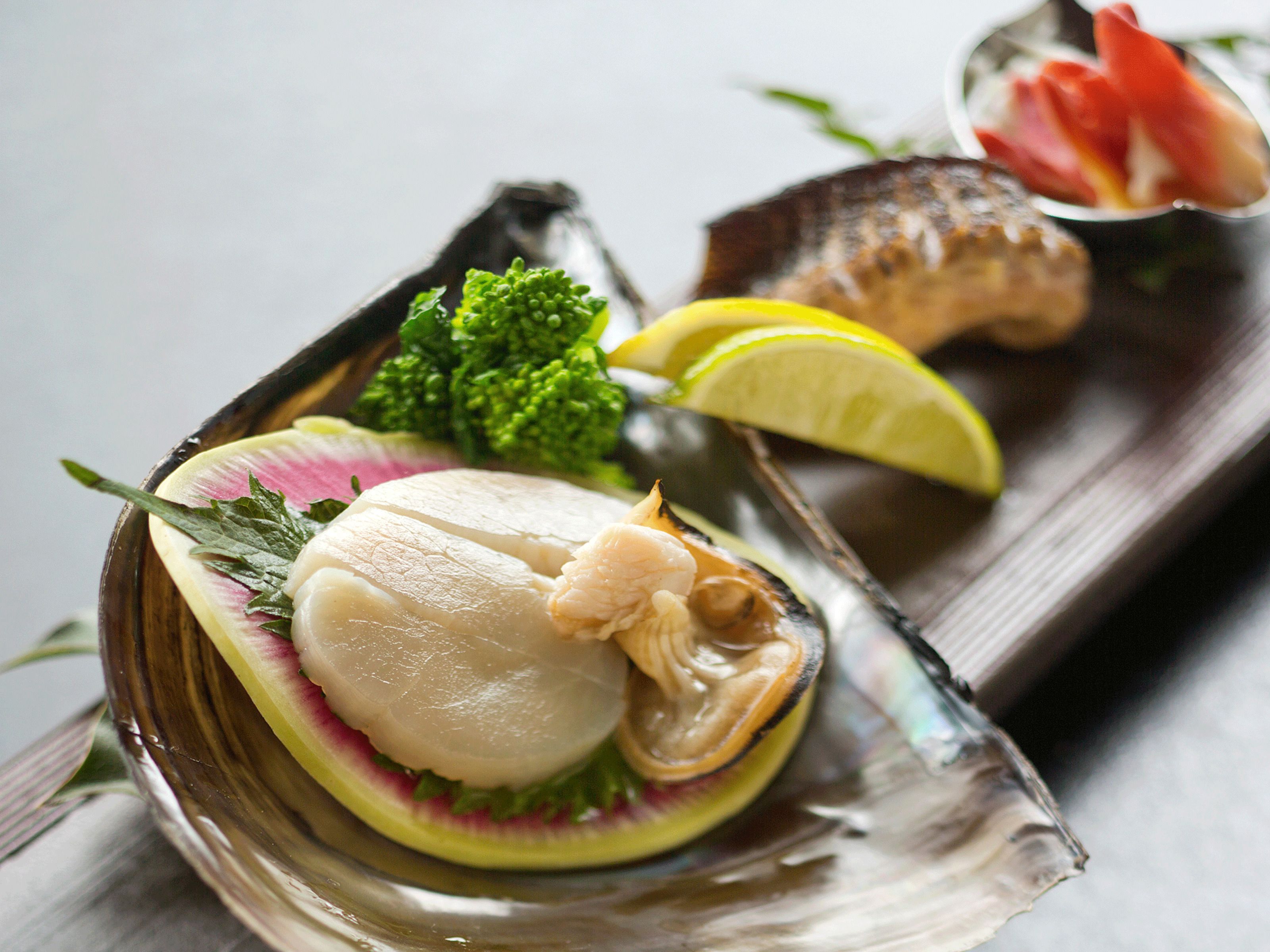 A seafood dish with a scallop, lemon, and parsley on a wooden board.