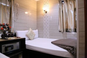 Habitación de hotel con una cama, una mesita de noche con un control remoto, un jarrón decorativo con flores y una lámpara fijada a la pared.