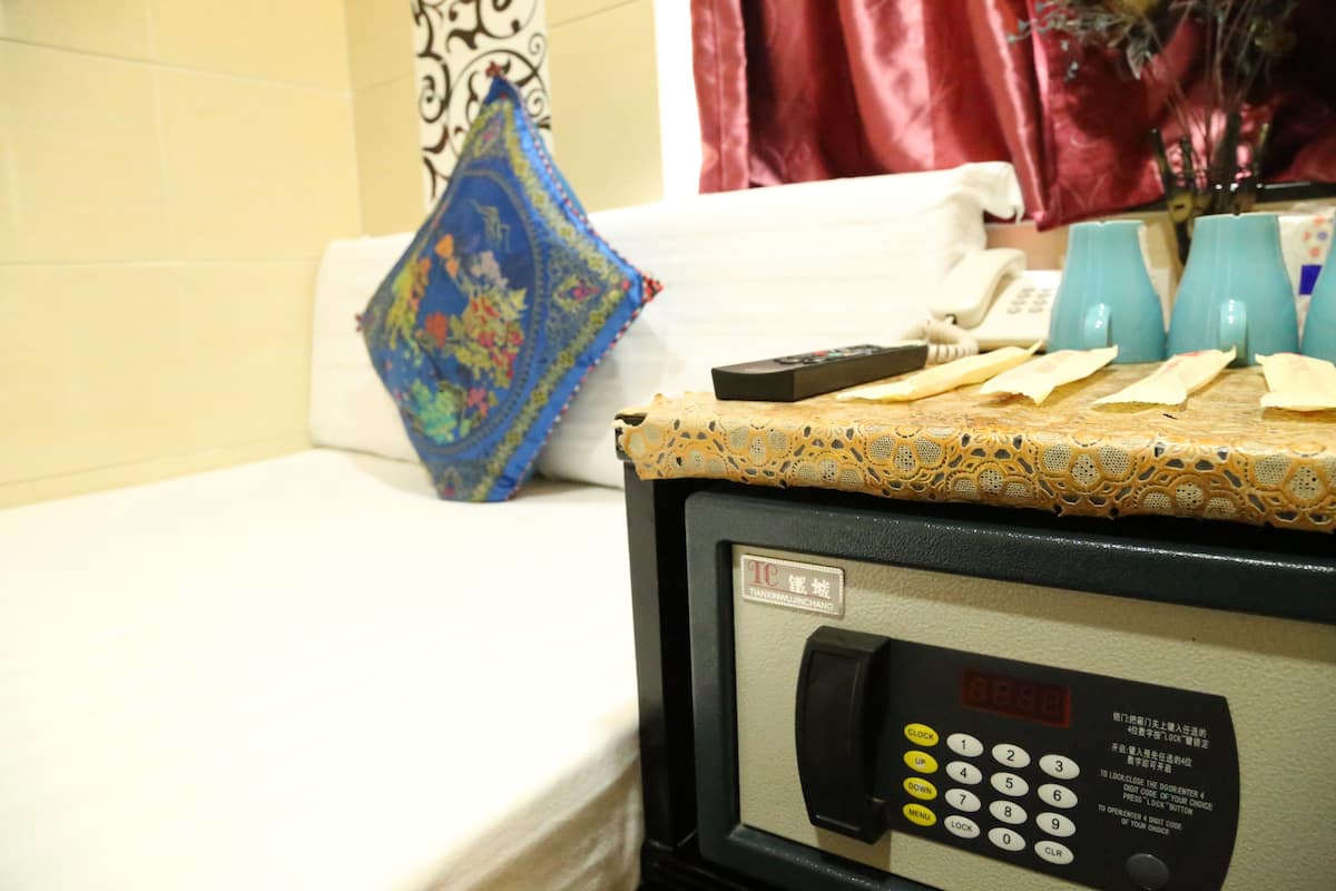A hotel room with a bed, a small table with a remote control, a phone, and a decorative pillow.