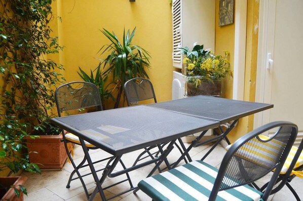 A patio with a metal table and chairs, surrounded by potted plants and yellow walls. - B&B Roma Borgo 91 (Rome)