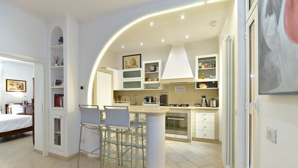 A modern kitchen with a central island, built-in shelving, and a dining area with bar stools. - B&B Roma Borgo 91 (Rome)