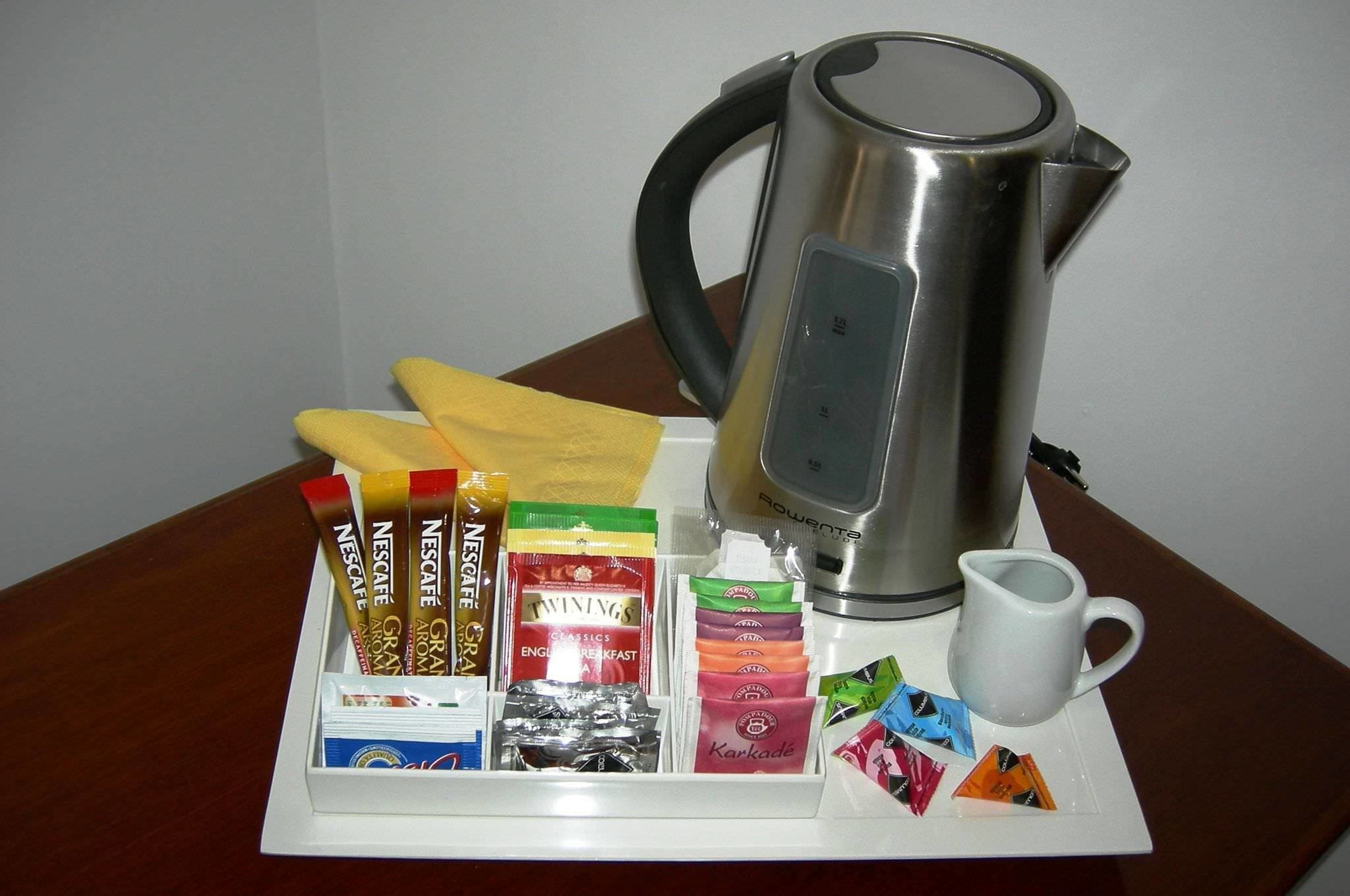 A tray with various coffee pods, a white mug, and a silver kettle on a table.