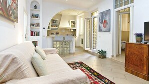 A modern living room with a sofa, a coffee table, and a TV on a wooden cabinet. There is a kitchen in the background with a bar and a dining area. - B&B Roma Borgo 91 (Rome)
