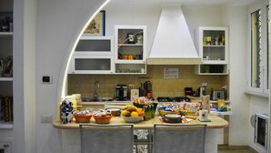A modern kitchen with white cabinetry, a central island with chairs, and various kitchen appliances. - B&B Roma Borgo 91 (Rome)