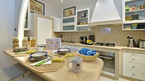 A modern kitchen with white cabinets, a gas stove, and a sink. There are various kitchen items on the counter, including a coffee maker, a kettle, and a basket of snacks. - B&B Roma Borgo 91 (Rome)