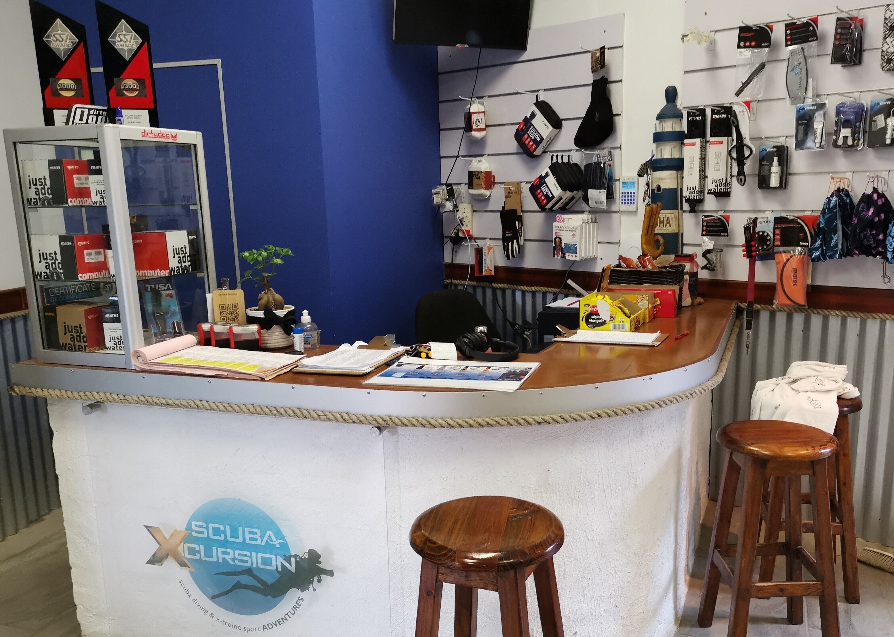 A counter with a logo for 'X SCUBA CURIOSITY' and a variety of diving equipment displayed on the wall.