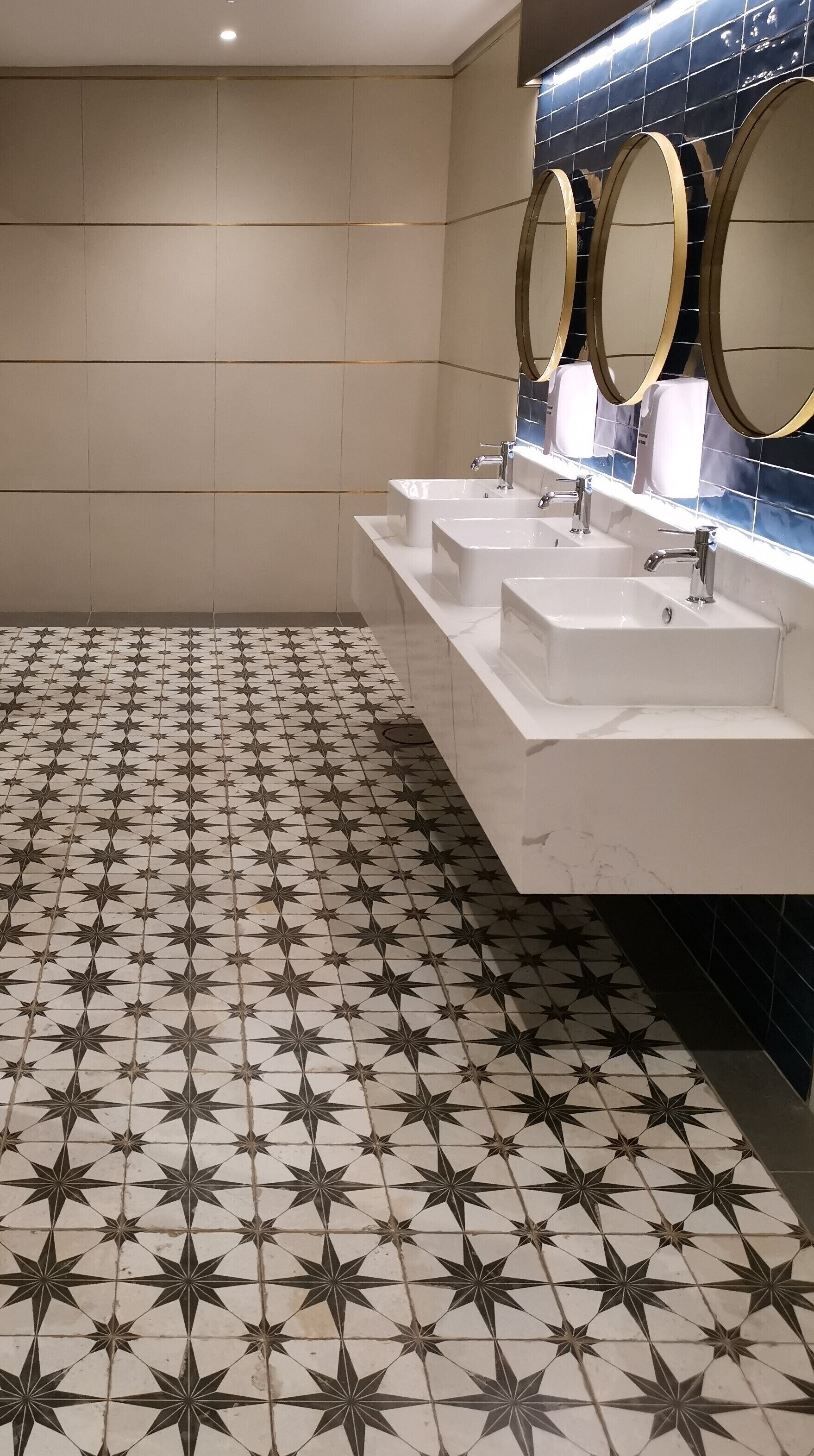Baño con tres lavamanos, piso de baldosas con diseño de estrellas y espejos montados en la pared.
