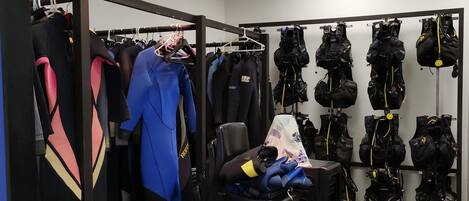 A storage room with rows of black diving gear, including wetsuits and backpacks, and a chair with blue gloves on it.