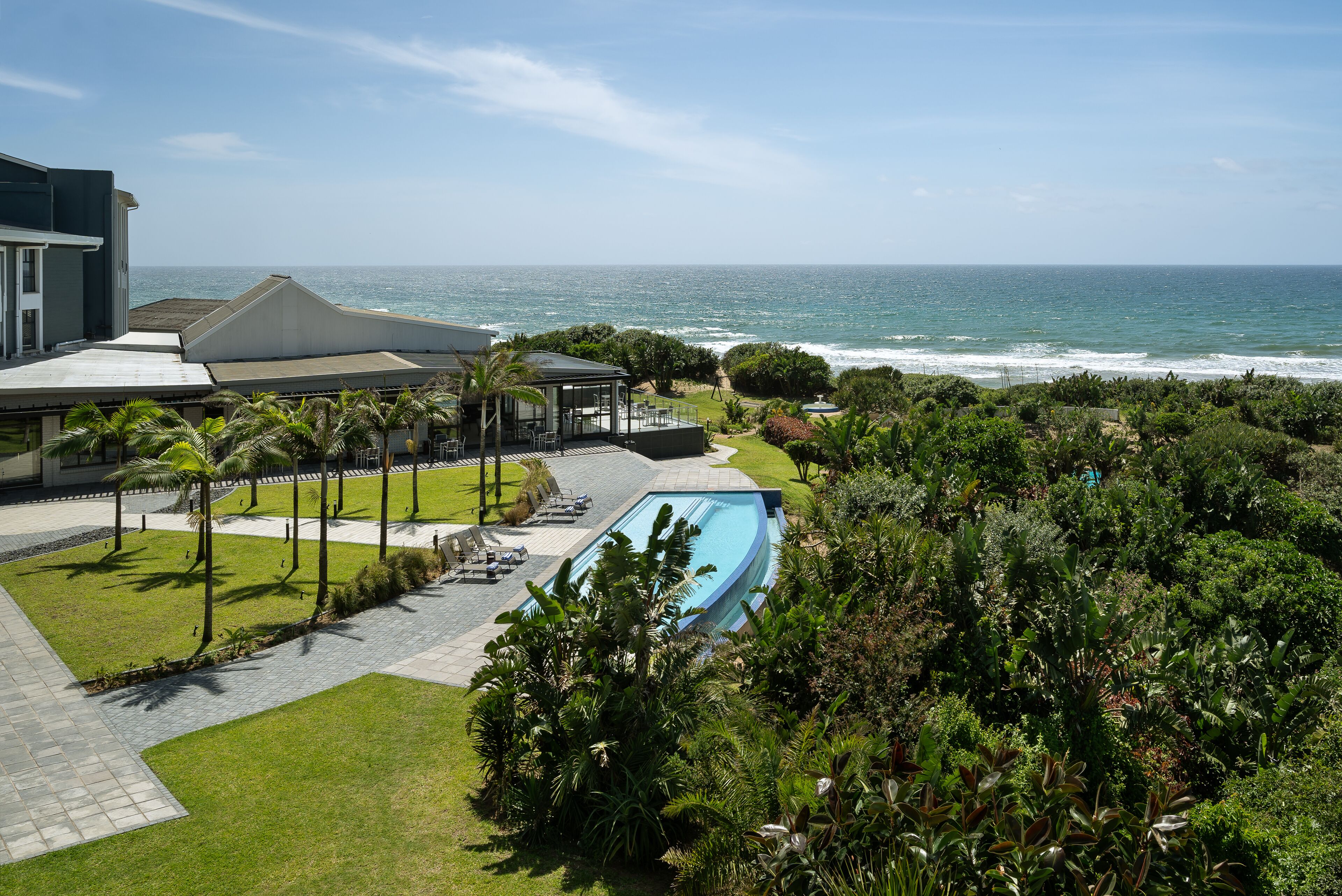A pool area with a view of the ocean, surrounded by lush greenery and a modern building.