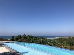 A rectangular swimming pool with clear blue water, surrounded by lush greenery and a view of the ocean. - Premier Resort Cutty Sark (Scottburgh)