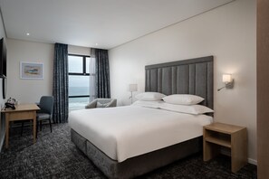 A modern hotel room with a large bed, a desk, a chair, and a view of the ocean. - Premier Resort Cutty Sark (Scottburgh)