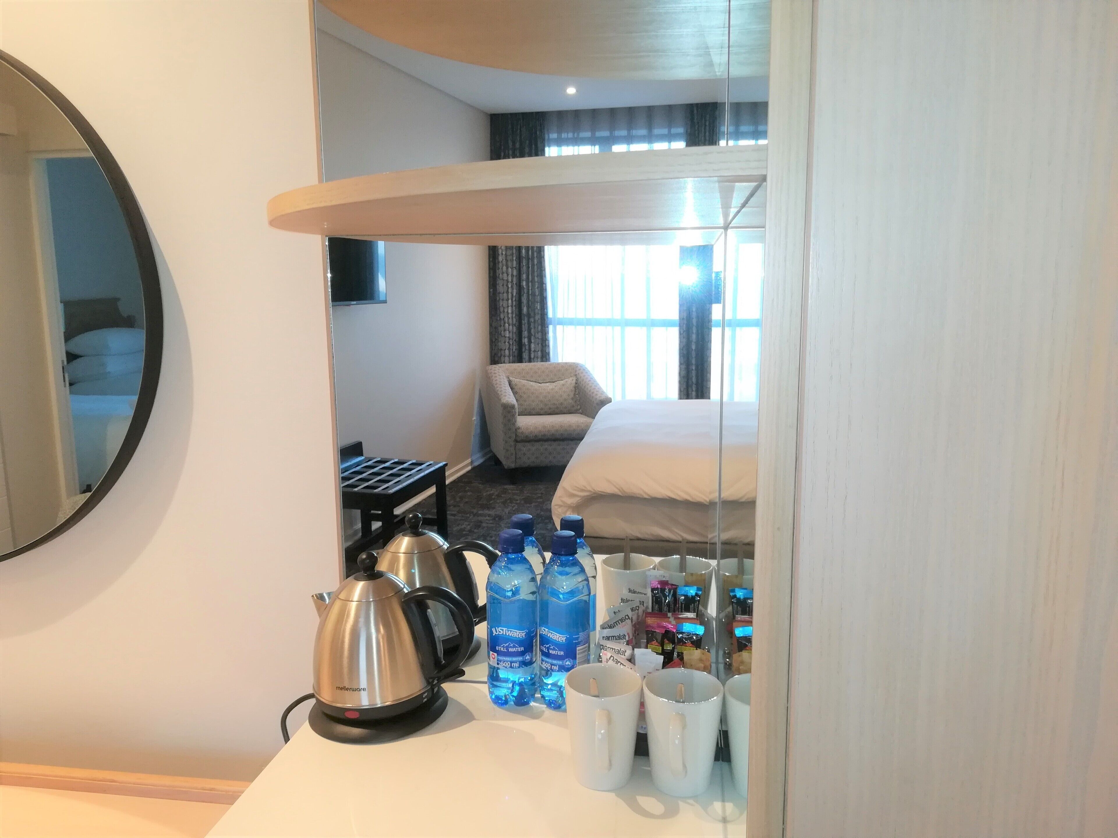 Una habitación de hotel con cama, sofá, cafetera y botellas de agua sobre la mesa.