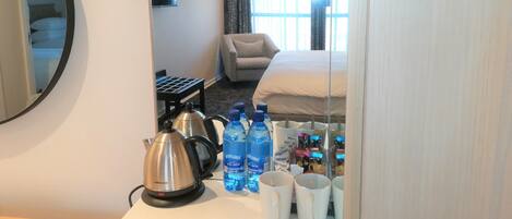 Una habitación de hotel con cama, sofá, cafetera y botellas de agua sobre la mesa.