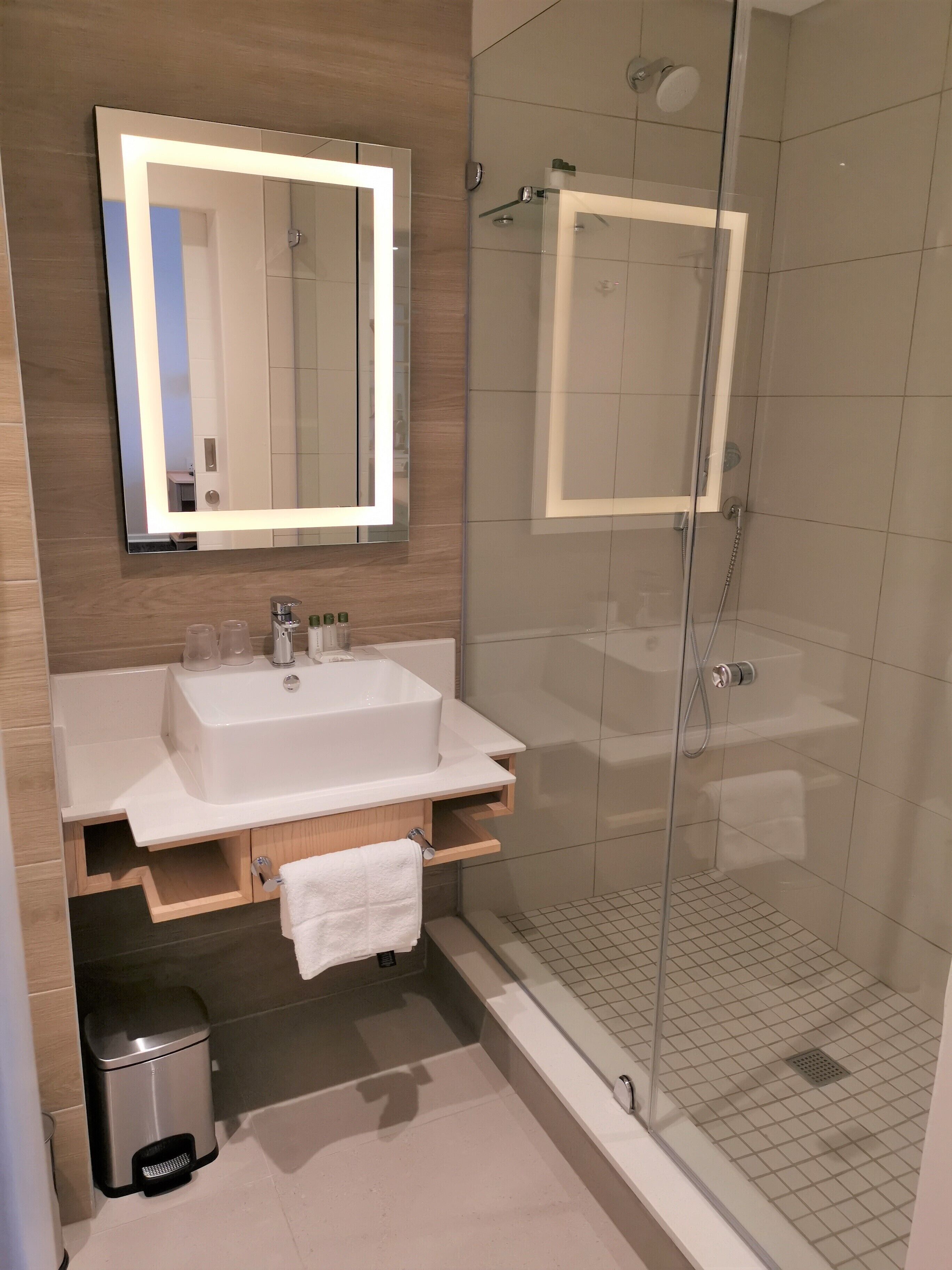 Ein modernes Badezimmer mit einem großen Spiegel, einem Waschbecken und einer Dusche mit Glaswand.