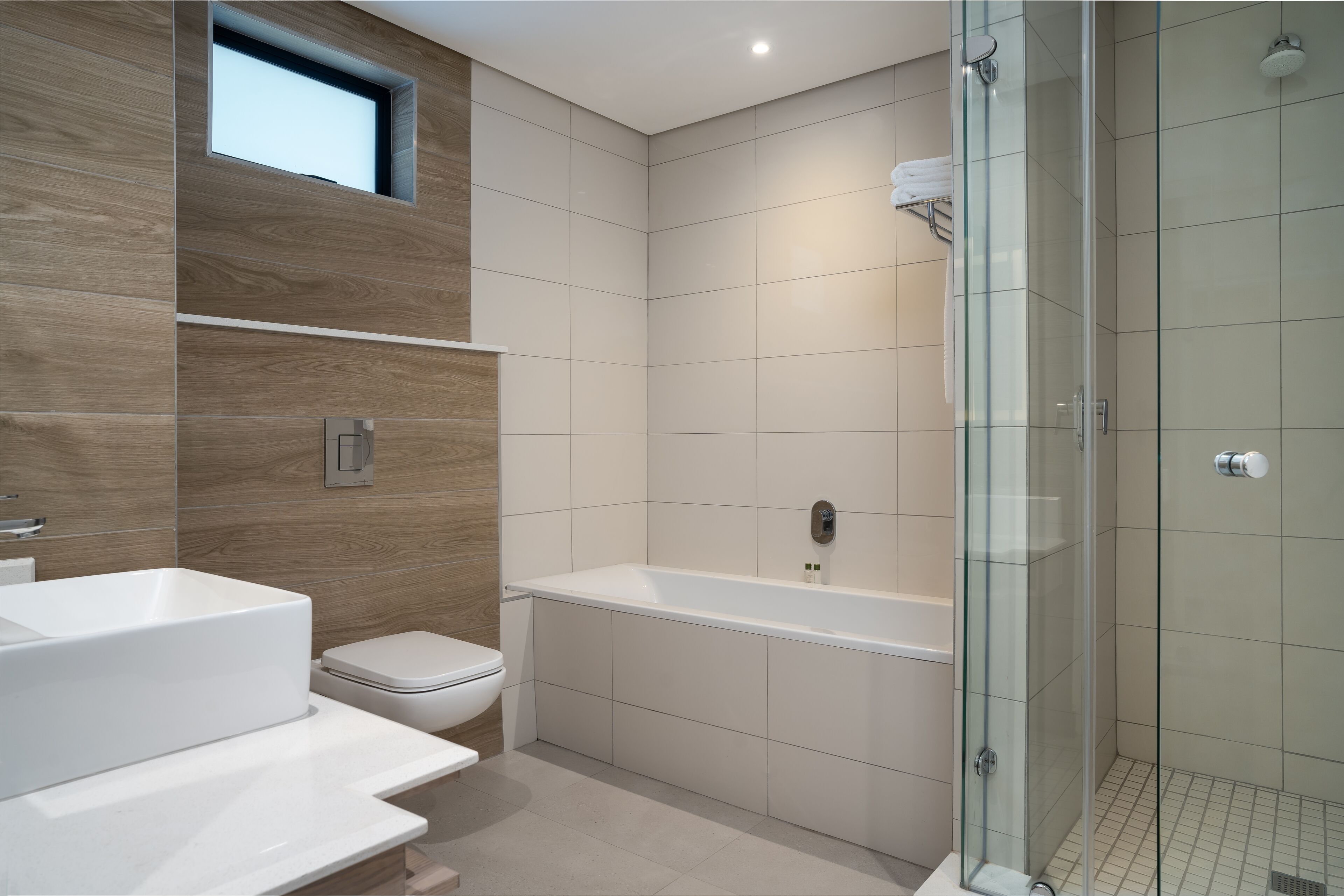 A modern bathroom with a bathtub, toilet, and glass-enclosed shower.