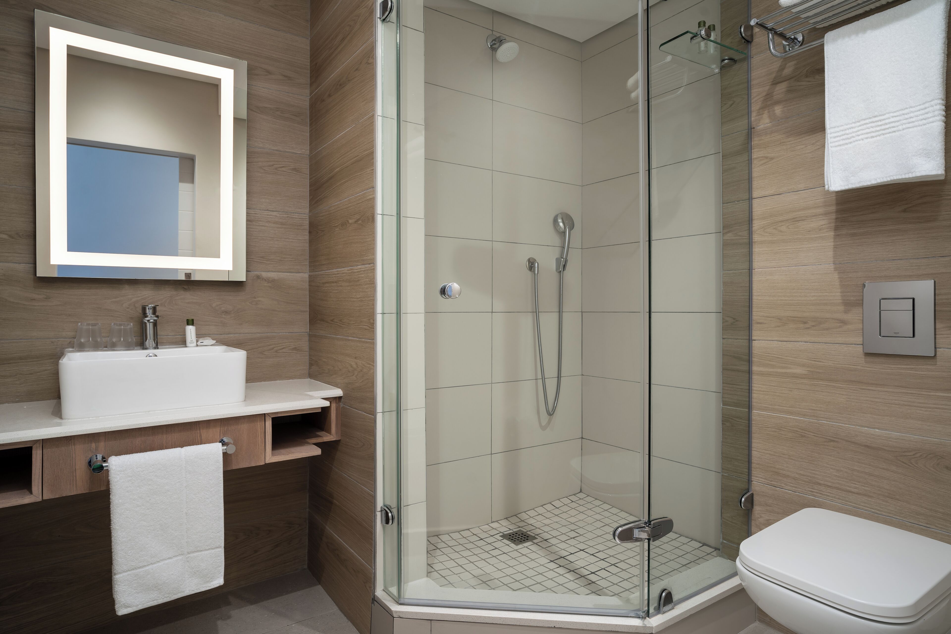 Un baño moderno con ducha envuelta en vidrio, un lavamanos blanco y un espejo sobre el mostrador.