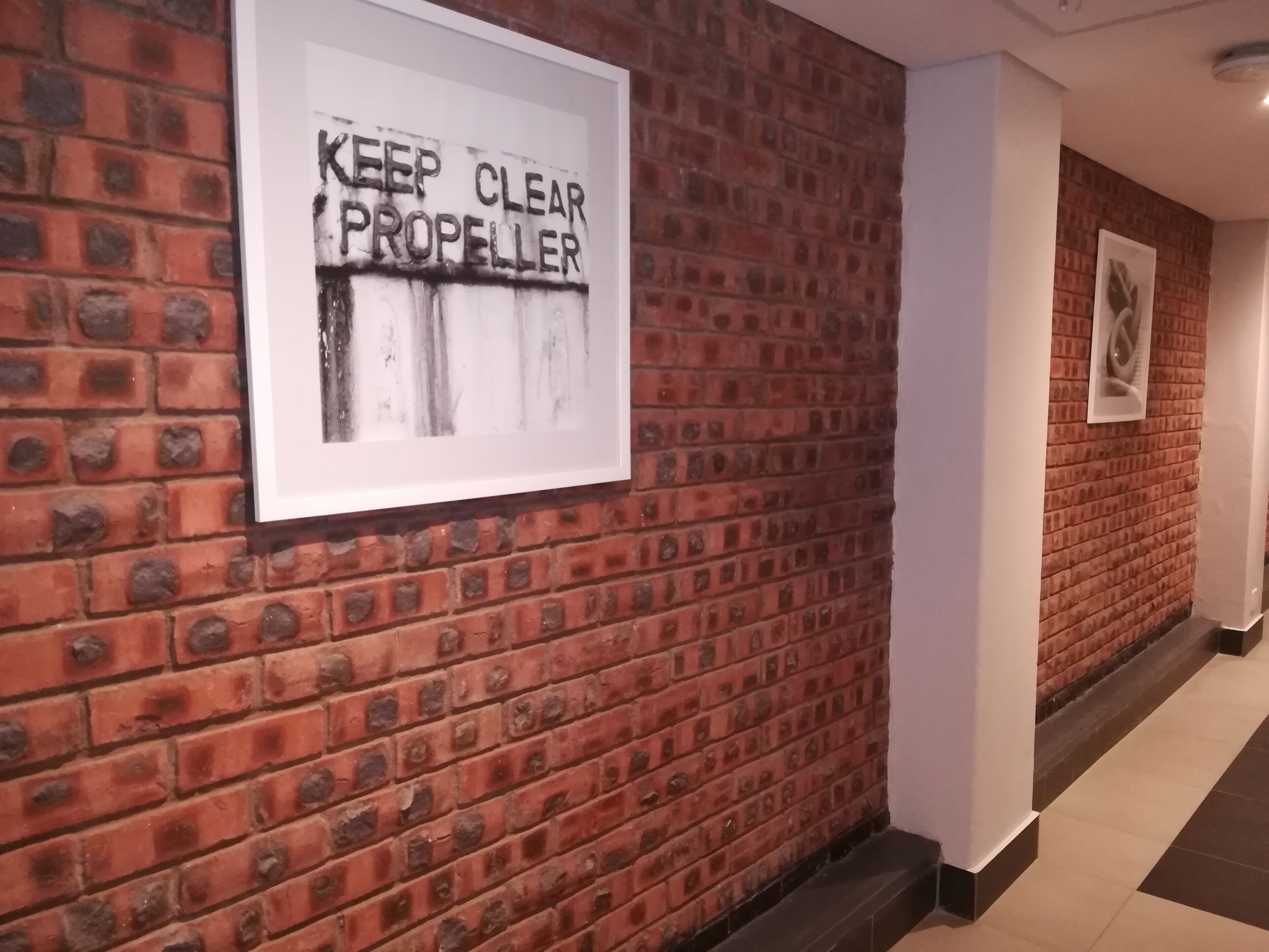 A hallway with a brick wall and a sign that reads "KEEP CLEAR PROPELLER".