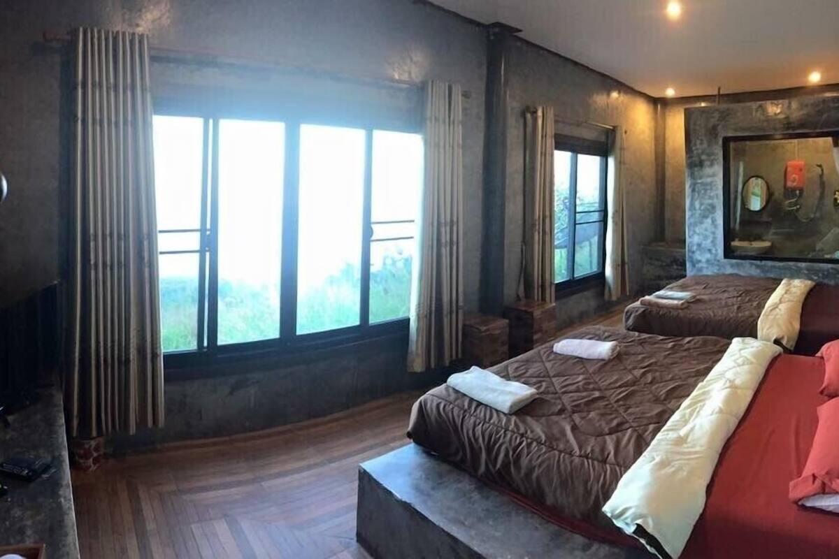 Une chambre avec une grande fenêtre, un lit, une table de chevet et un tableau accroché au mur.