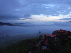 A high-altitude view of a mountainous area with a house surrounded by greenery and a misty valley below. - Seemok Resort (Khao Kho)