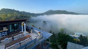 A restaurant with outdoor seating overlooking a valley shrouded in mist. - Seemok Resort (Khao Kho)