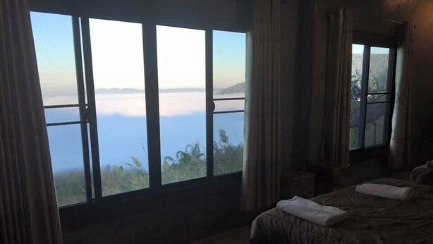 A bedroom with a large window overlooking a body of water, a bed, and a nightstand. - Seemok Resort (Khao Kho)