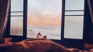 A person lying in bed with a view of a beach and ocean through a window. - Seemok Resort (Khao Kho)