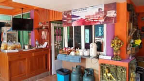 A small coffee shop with a wooden counter, a TV mounted above it, and various items like a kettle, cups, and a Buddha statue. - Seemok Resort (Khao Kho)