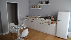 A compact kitchen with white cabinetry, a white refrigerator, and a dining area with a white table and chairs. - Room 56 (Bari)