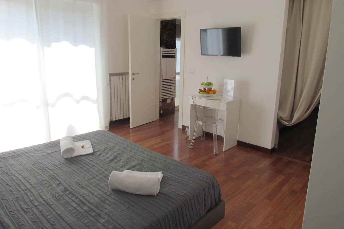 A hotel room with a bed, a desk, a chair, a television, and a radiator.