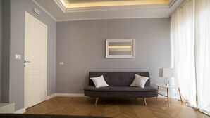 A modern room with a grey sofa, a small white table, and a bed. - Room 56 (Bari)
