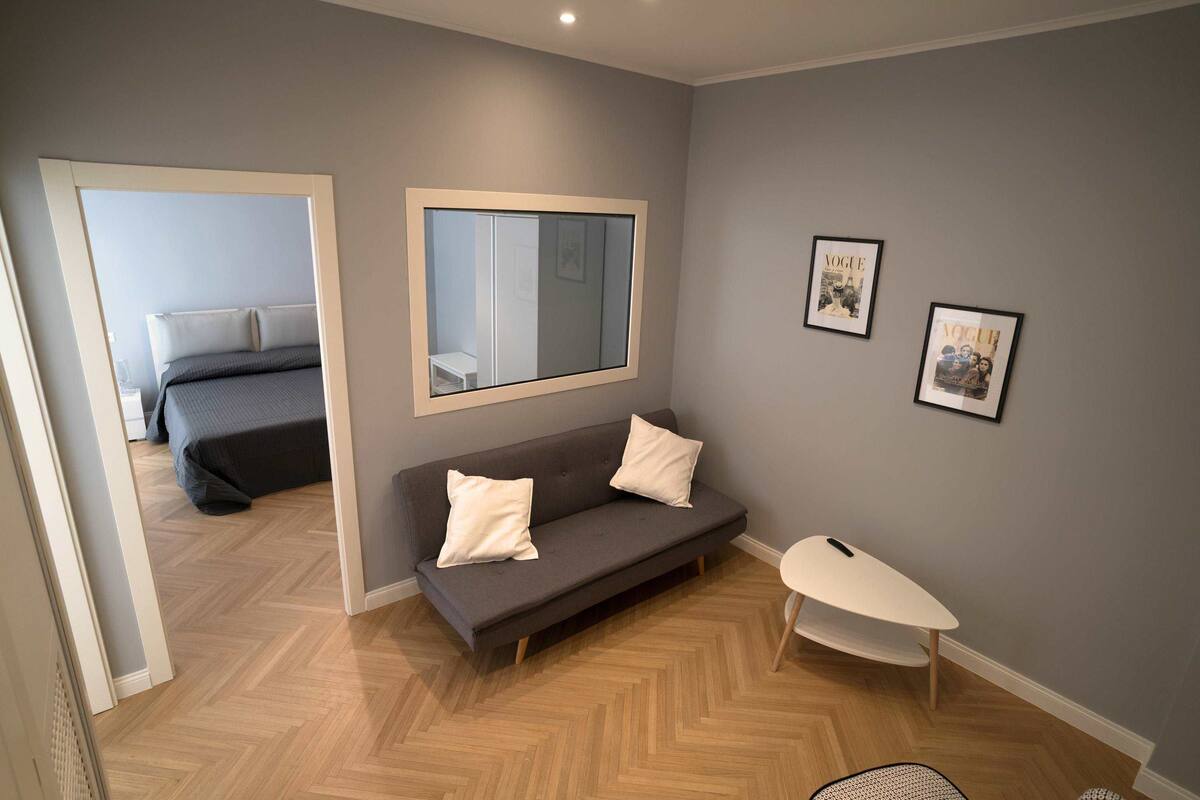 A modern room with a grey sofa, a small white table, and a mirror on the wall.