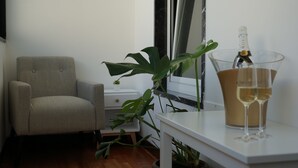 A room with a grey armchair, a white table with a bottle and glasses, and a potted plant. - Room 56 (Bari)